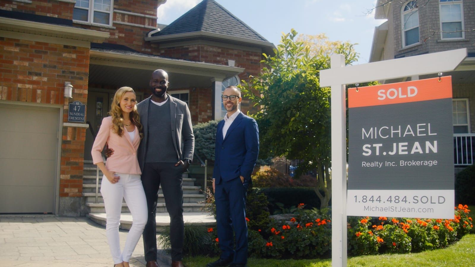 Three Michael St. Jean Realty agents beside a Sold sign in front of a brick home